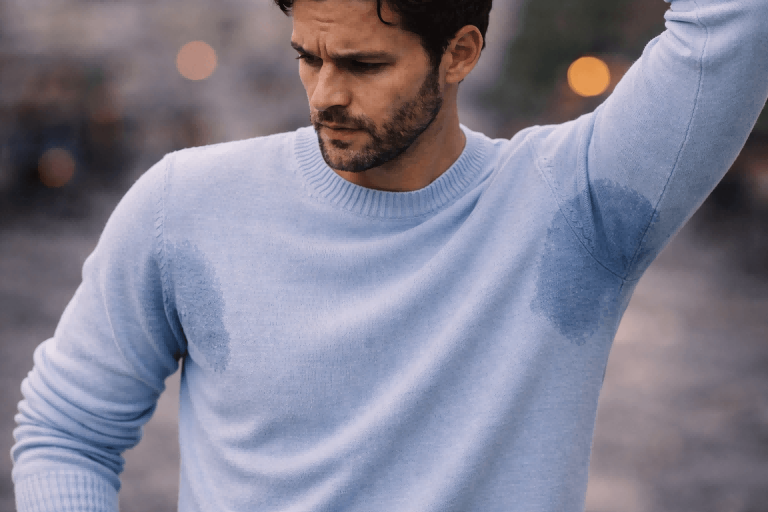 A man in a light blue cotton sweater with visible sweat marks under the arms.