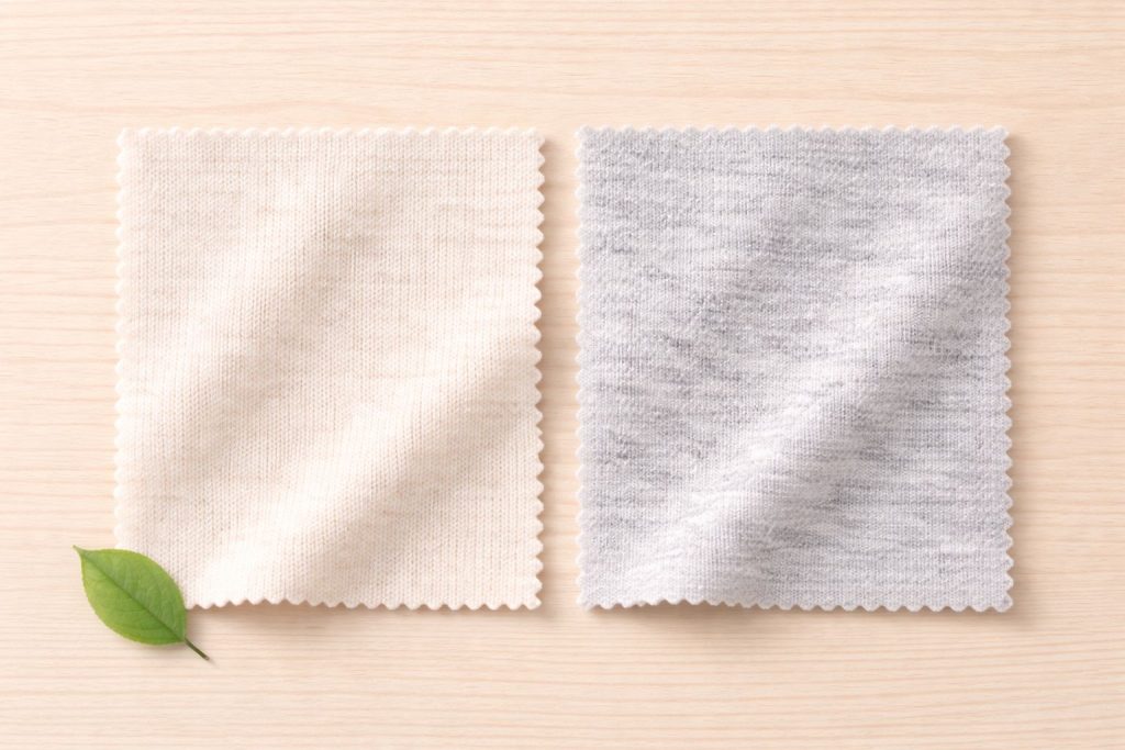 Flat lay Organic cotton swatch and merino wool swath side-by-side. Clean light wood surface. Small green leaf. Neutral colors, top-down, soft diffused light.