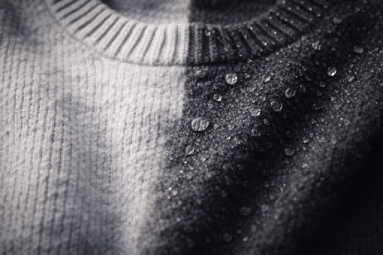 Macro photo of a cotton sweater, half dry and soft, the other half dark and wet with water droplets. Dramatic side light.