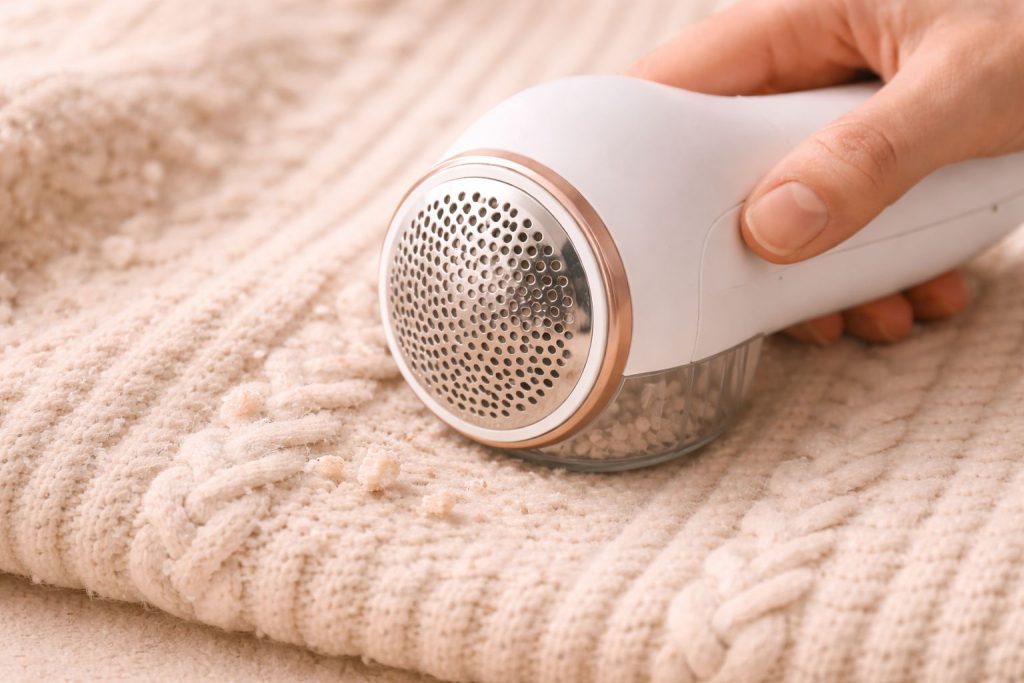 Close-up of knitwear pilling removal with fabric shaver, clean neutral background, premium minimal editorial style, soft warm light, realistic