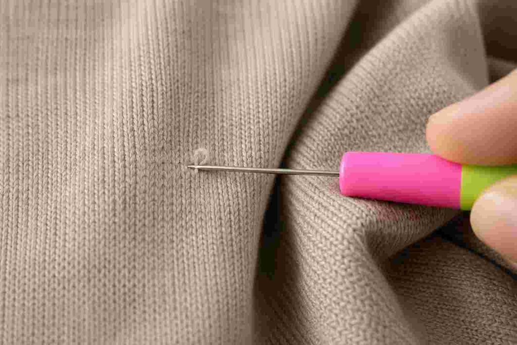 Macro shot of a snag repair needle carefully pulling a loose thread back into a fine-knit sweater